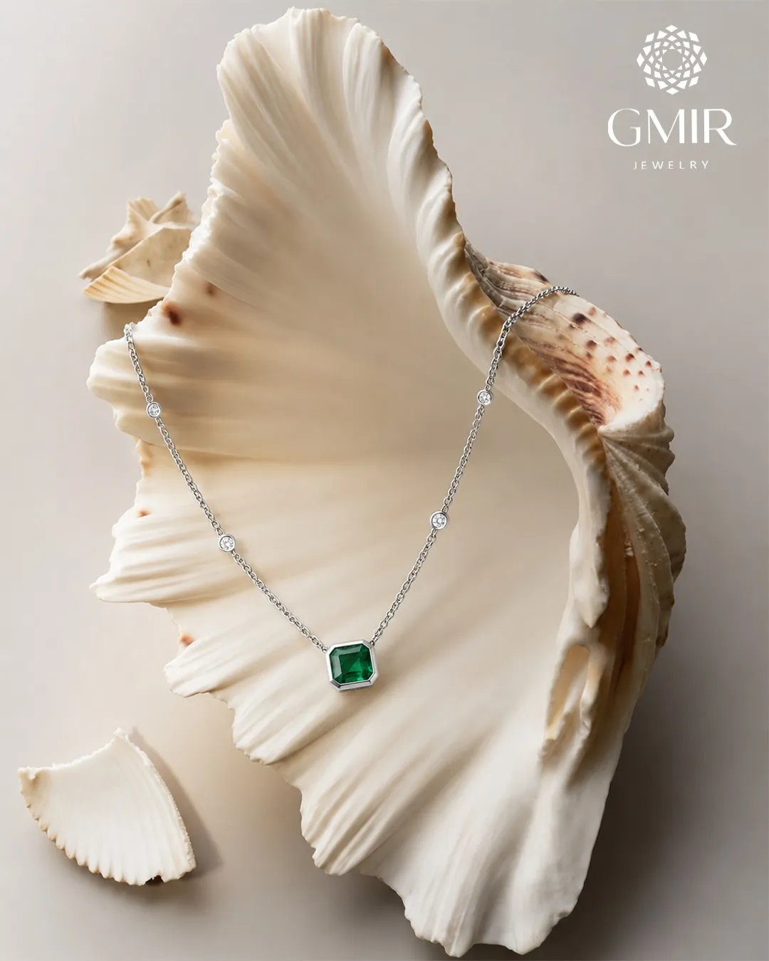 Collier en or blanc serti de diamants et d’une pierre verte, posé dans un coquillage
